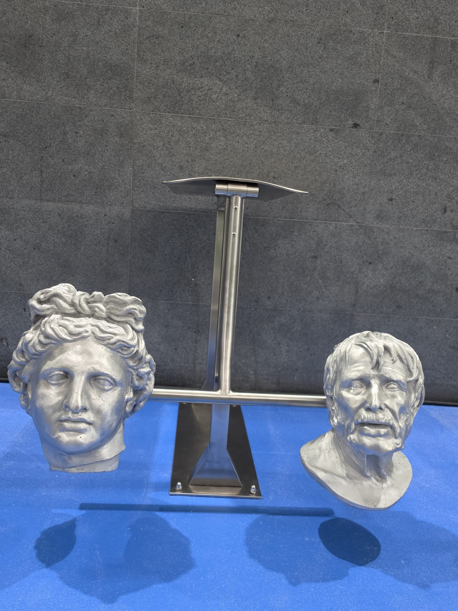Dettaglio: due teste classiche argentate, una giovane dai capelli ricci e una di un uomo anziano con la barba, ai lati di un attrezzo in acciaio