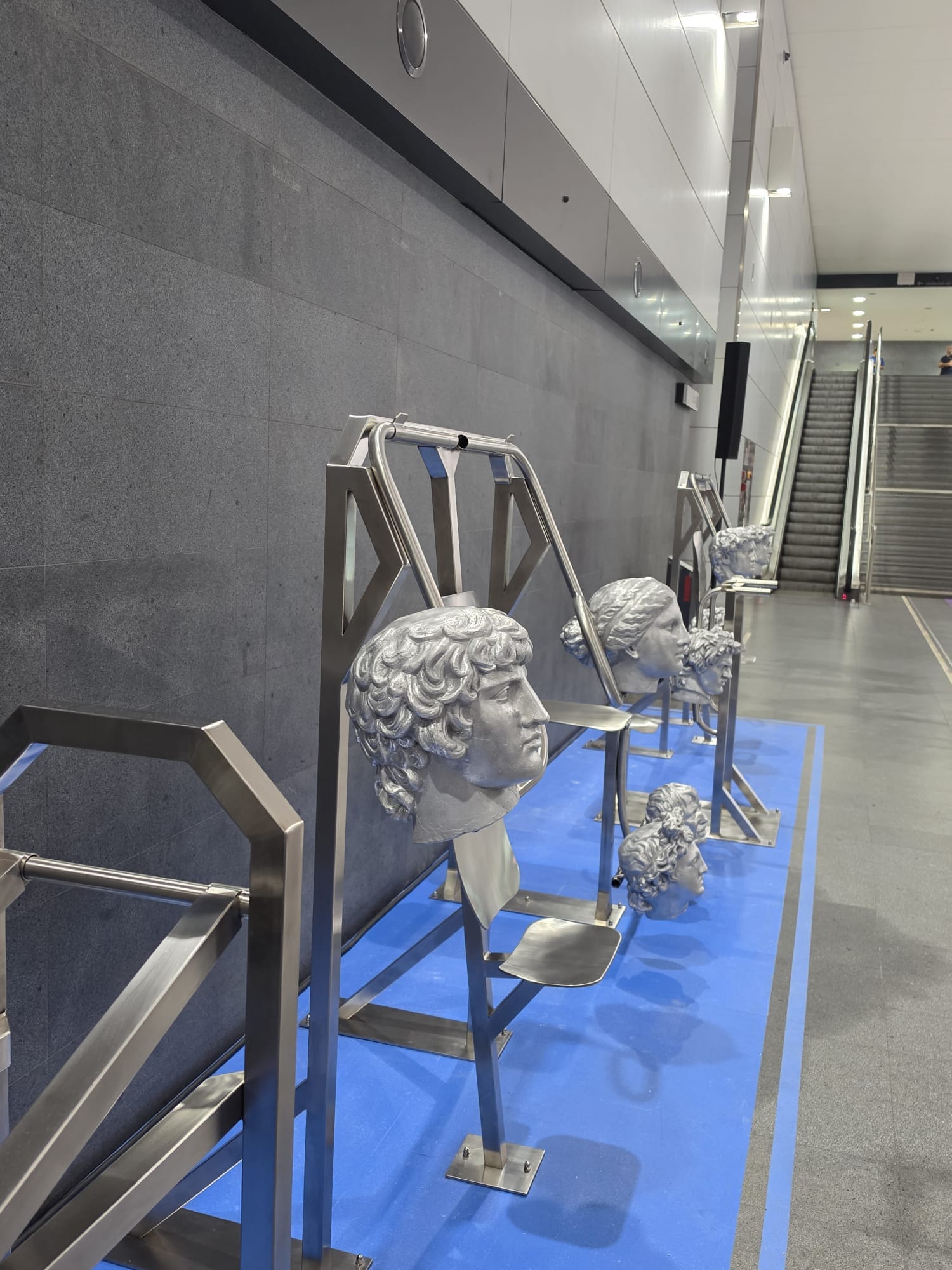 Physical Culture: Metro Edition: attrezzi da palestra in acciaio con teste classiche argentate, allineati sulla pedana blu lungo la parete